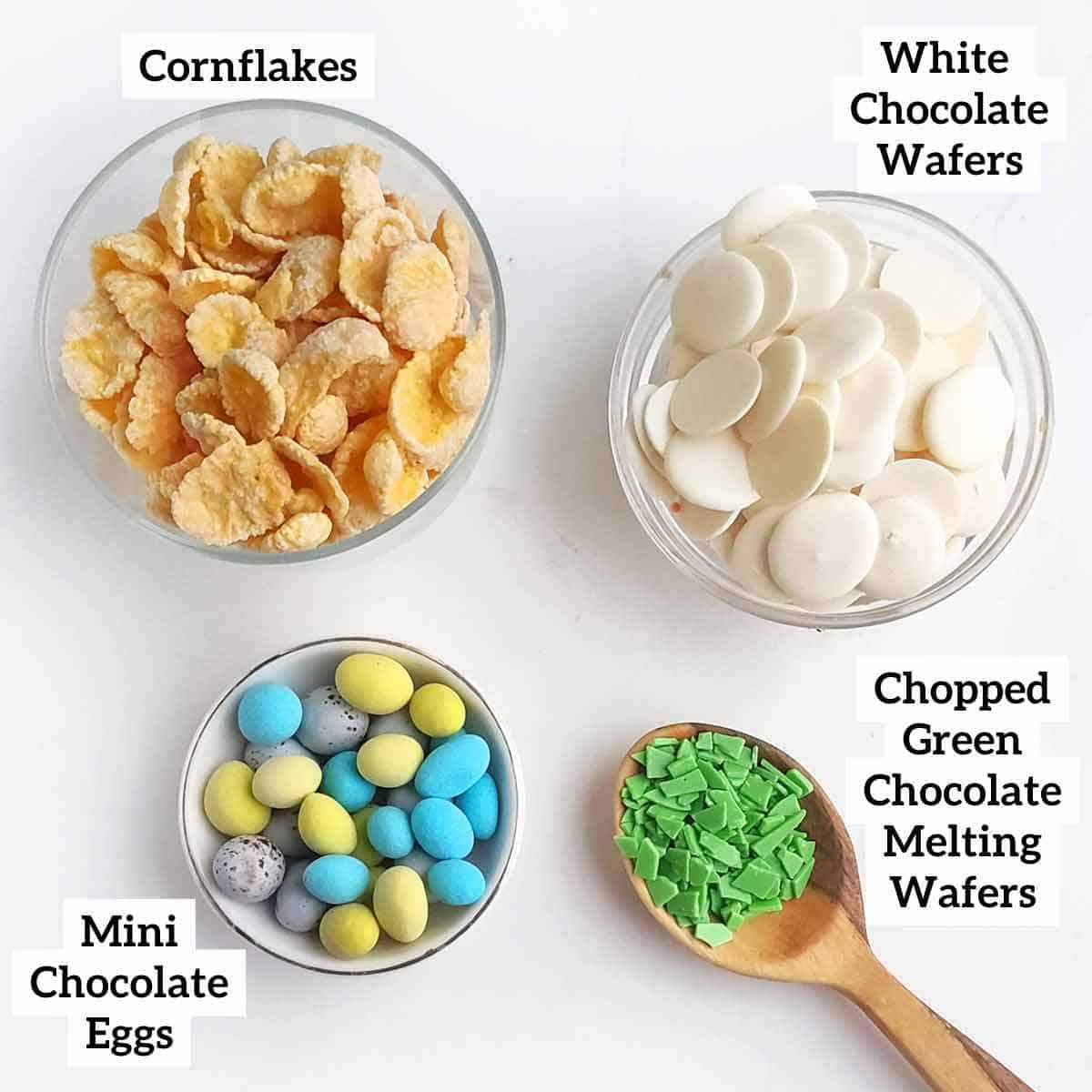 Cornflakes, white chocolate wafers, chopped green chocolate melting wafers, and a bowl of mini chocolate eggs.