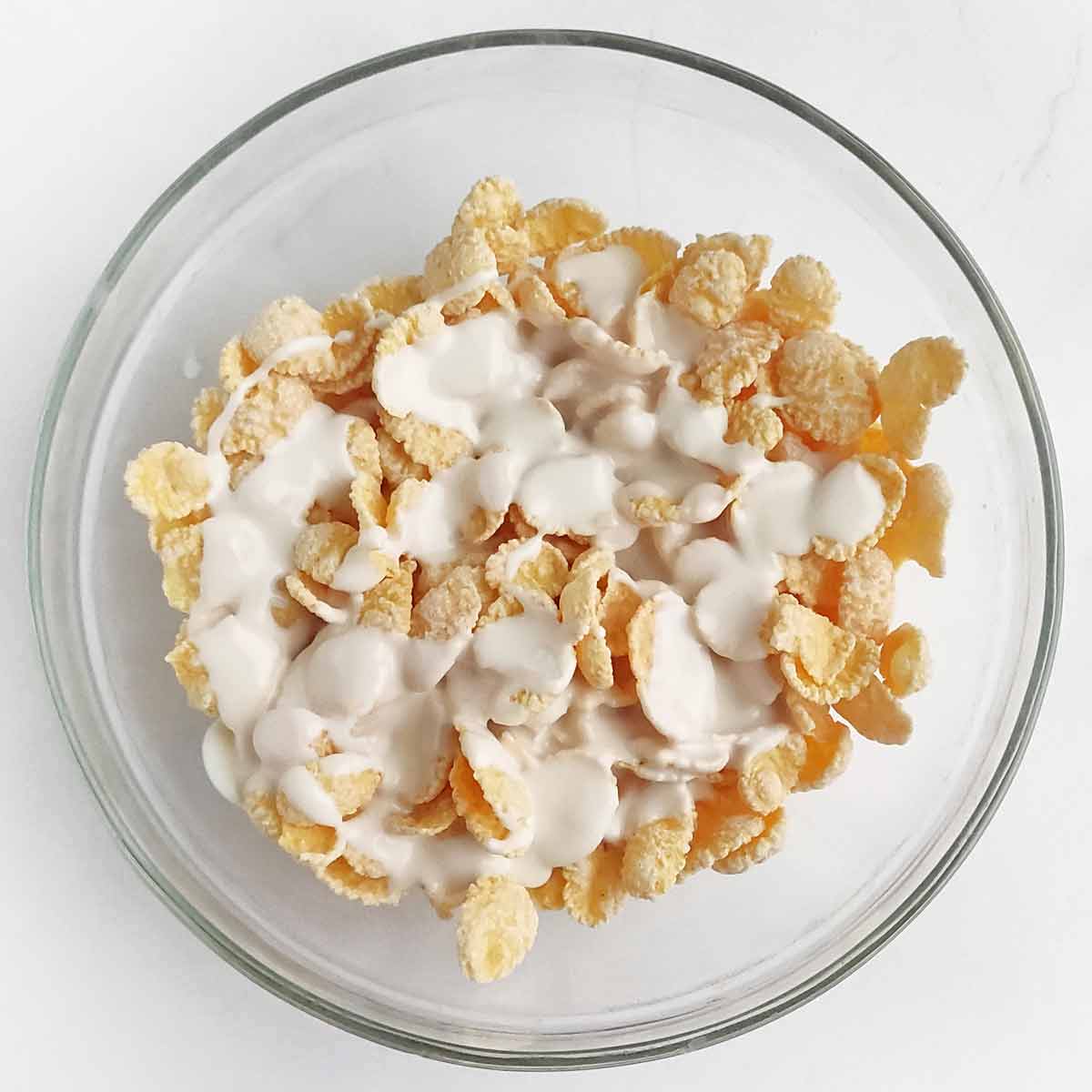 A glass bowl with cornflakes and melted white chocolate.