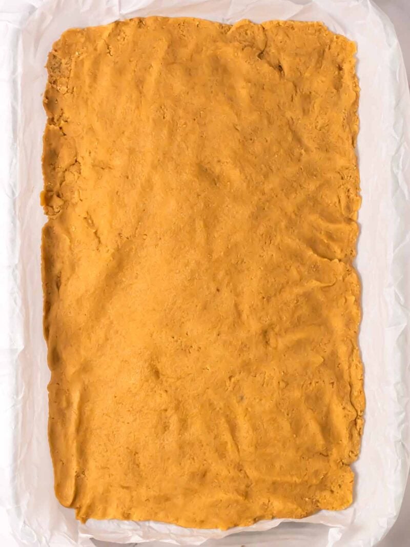 First layer of cookie dough in 9 by 13 inch glass baking dish.