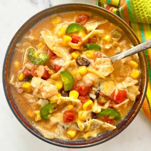 Creamy chicken tortilla soup in a brown serving bowl with a spoon.
