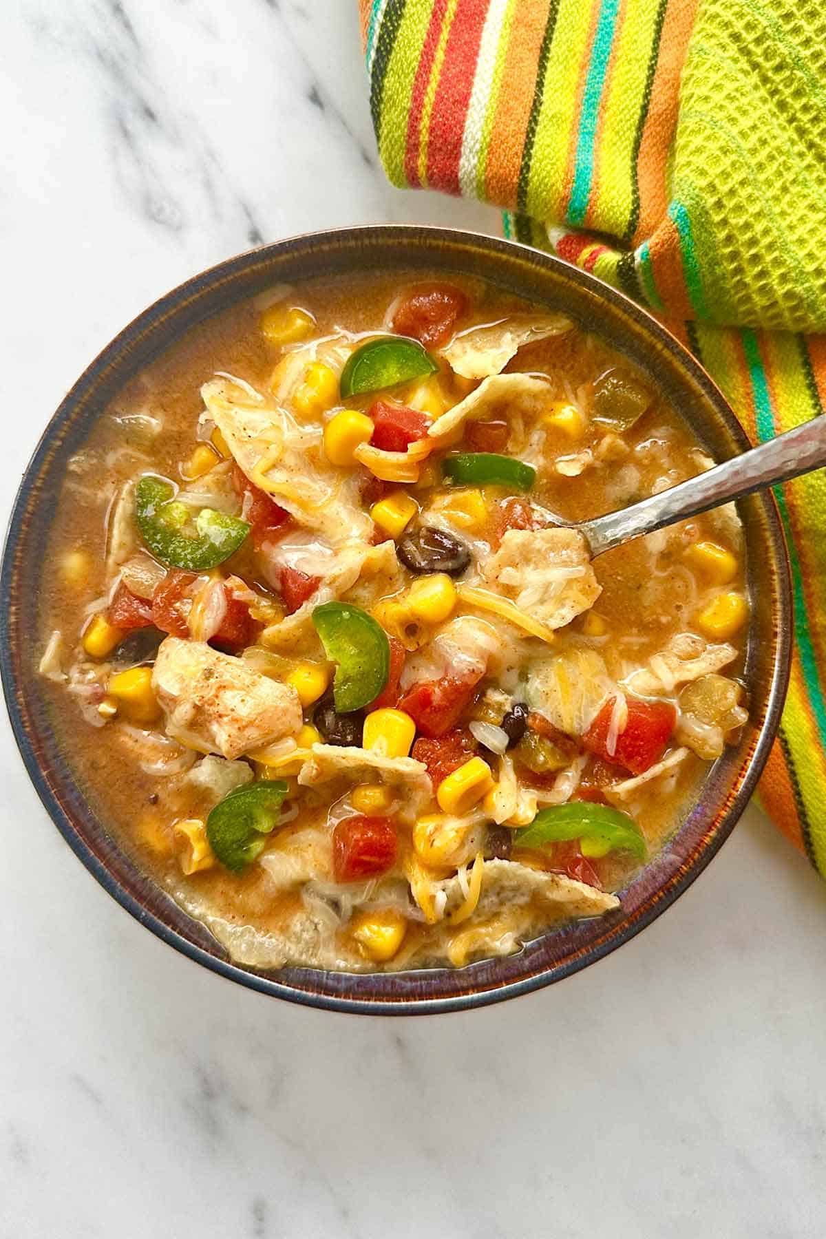 Bowl of chicken tortilla soup with a spoon and a folded towel.
