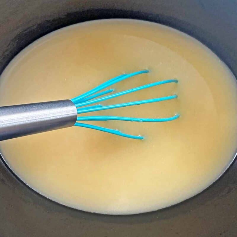 Whisking together chicken broth and cream of chicken soup in a crock pot.