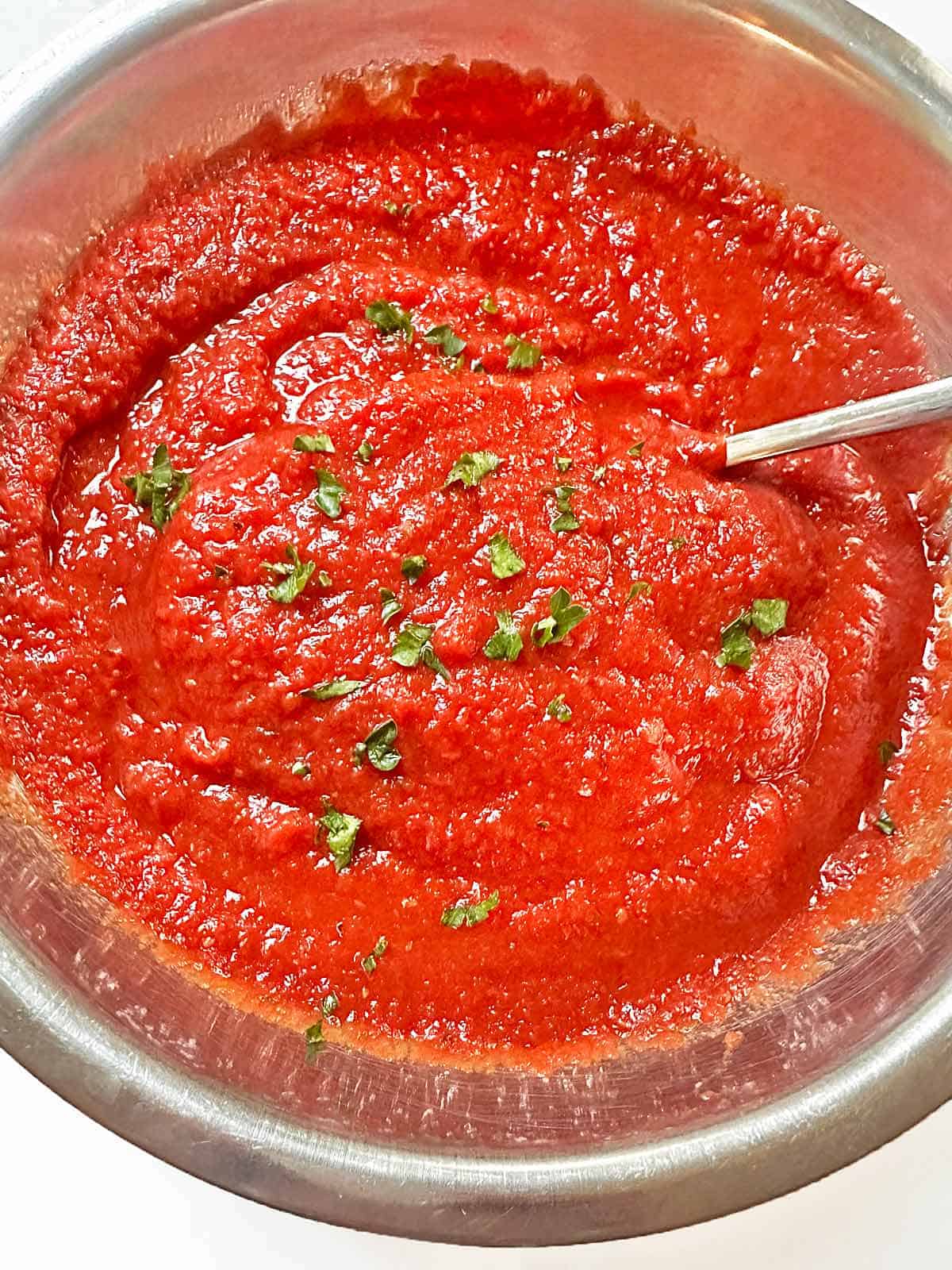 Close up of a bowl of homemade pizza sauce with a serving spoon.