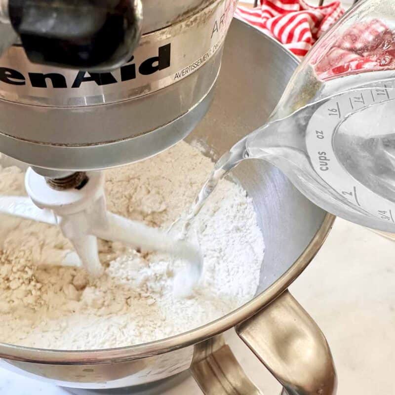 Pouring water into the dough ingredients in a stand mixer bowl.