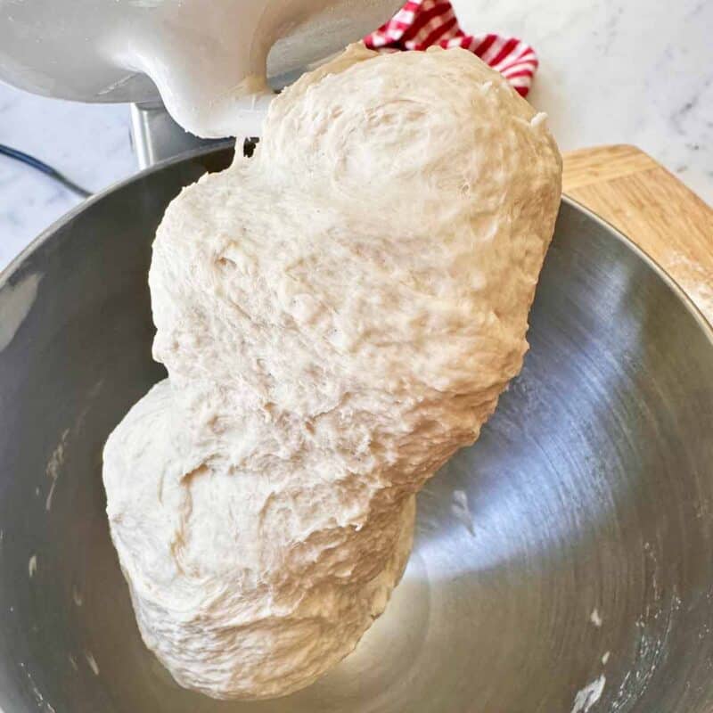 pizza dough on the dough hook in a mixing bowl.
