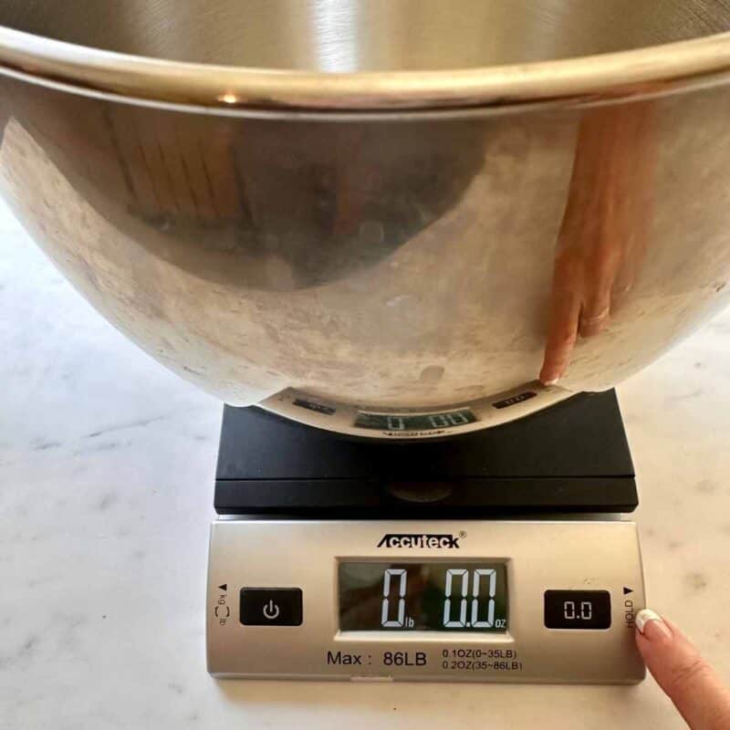 An empty stainless steel mixing bowl on a scale for weighing flour.