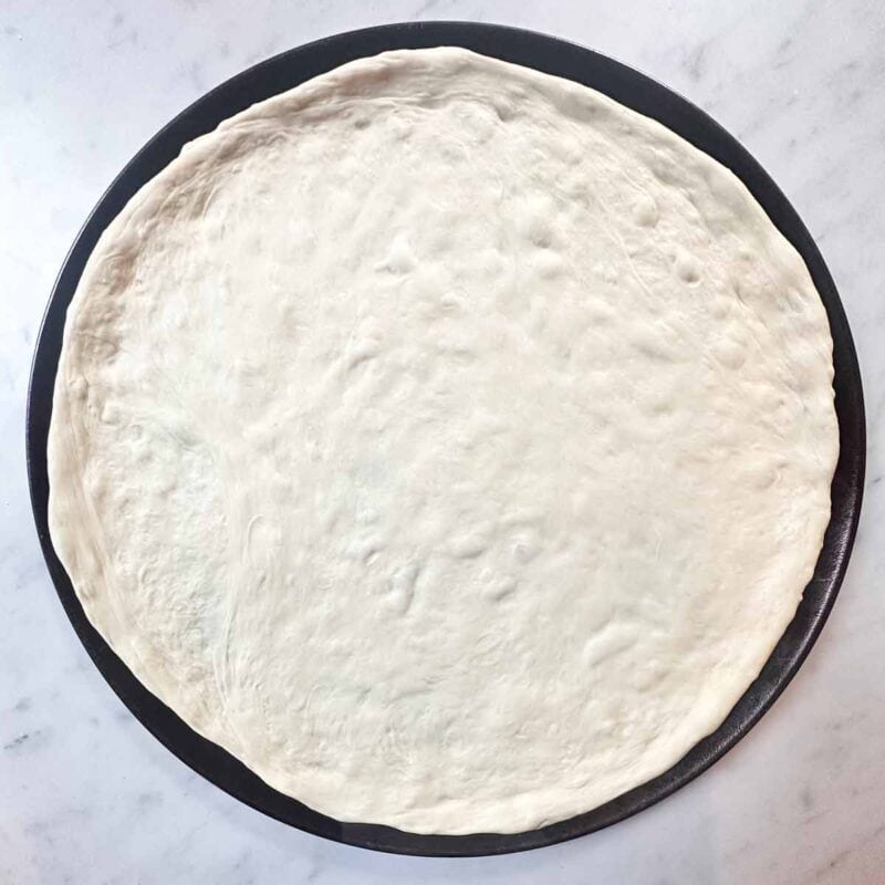 Round pizza pan with uncooked pizza dough, ready to bake.