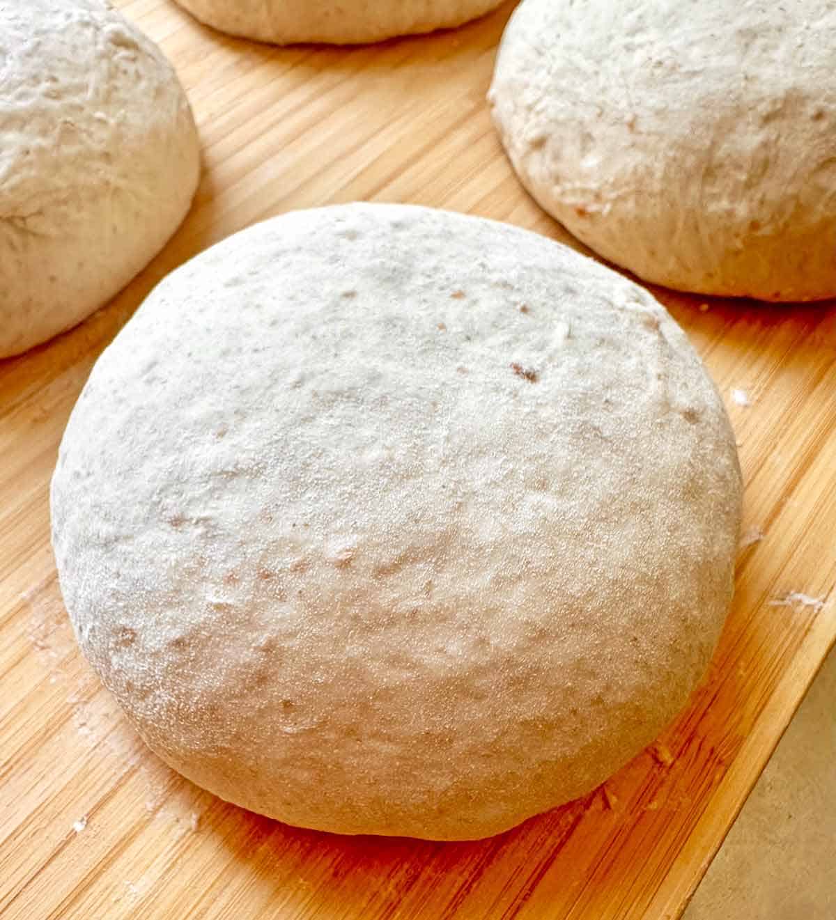 Spelt flour pizza dough balls on a bamboo cutting board.