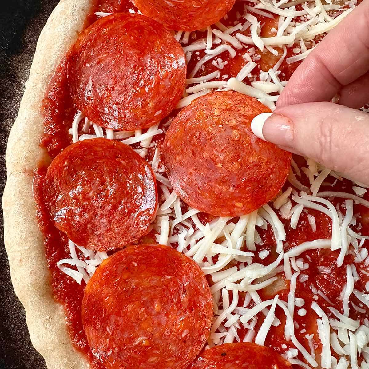 Arranging the pepperoni slices on the pizza.