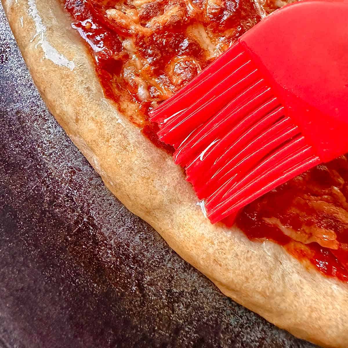Brushing garlic butter on hot pizza crust.