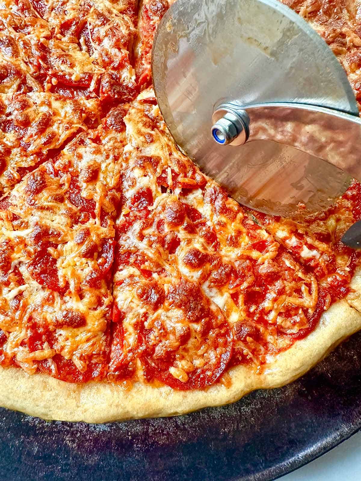 Cutting a home-baked pizza with a pizza cutter.