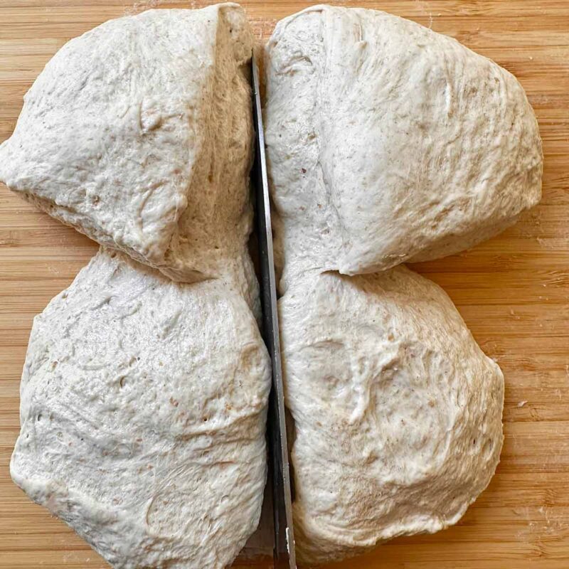 Using a kitchen knife to cut pizza dough in 4 portions.