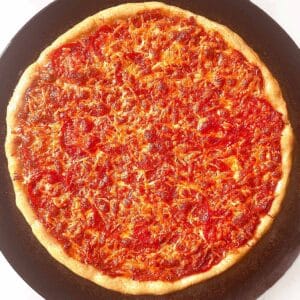 Homemade pepperoni pizza on a black pizza pan, ready to cut and eat.