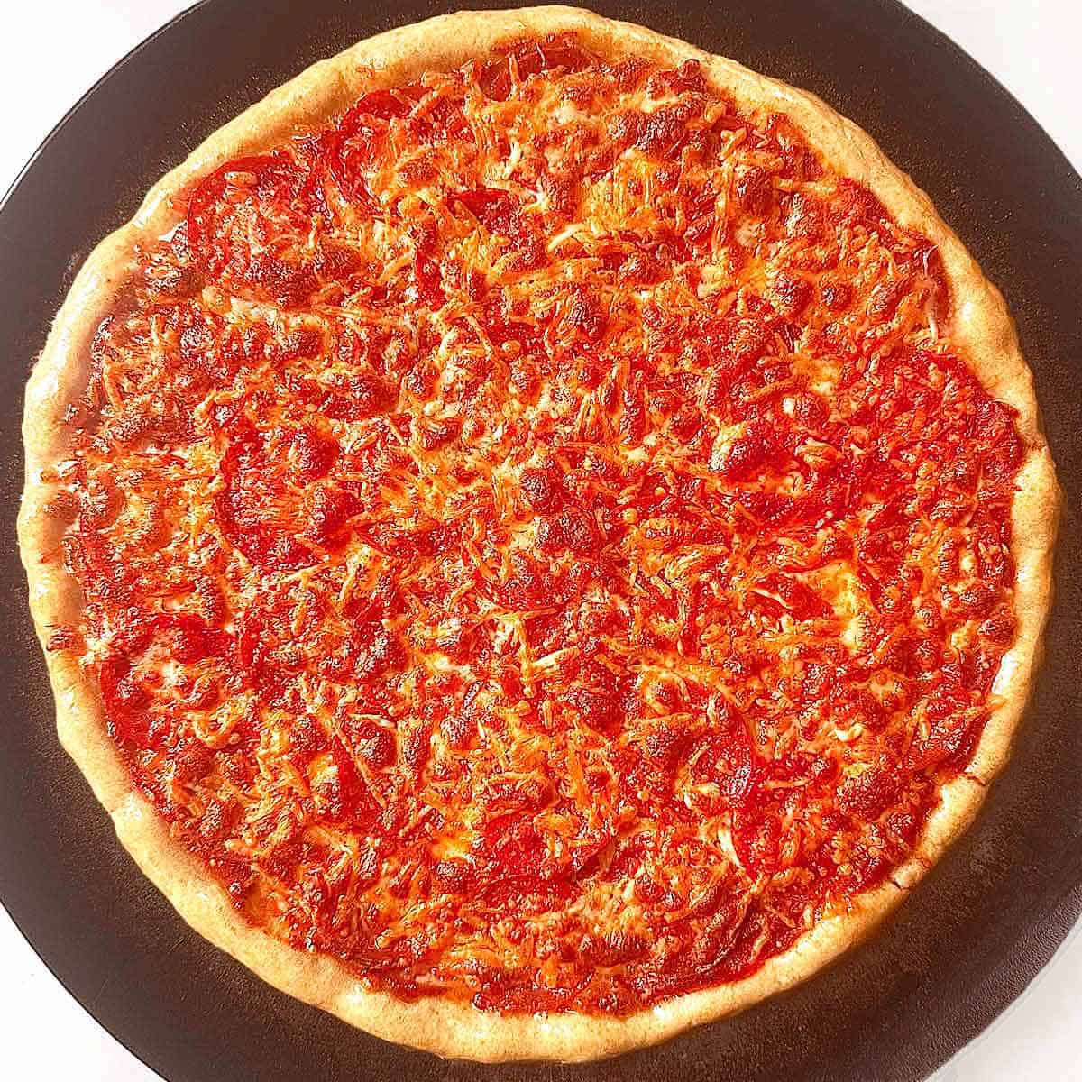 Homemade pepperoni pizza on a black pizza pan, ready to cut and eat.