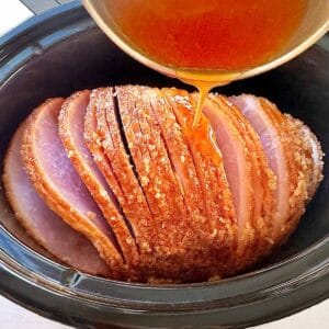 Pouring honey glaze sauce over a spiral ham in a slow cooker.