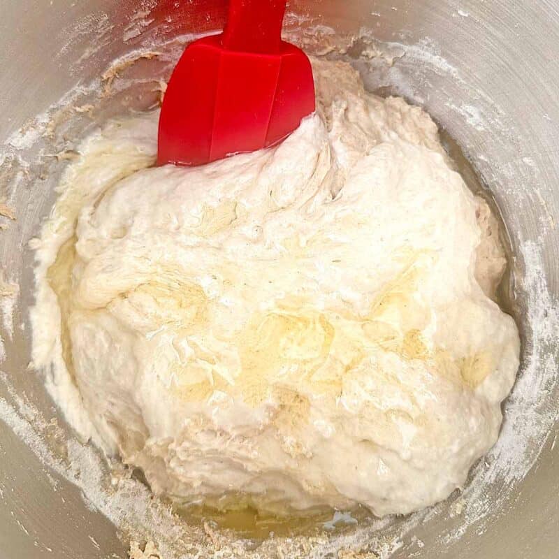 Mixing pizza dough in a bowl with a red spatula.