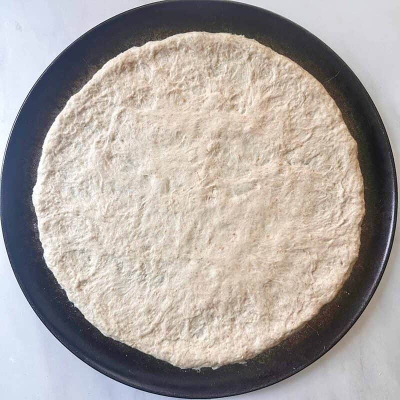 A round pizza pan with uncooked pizza dough.