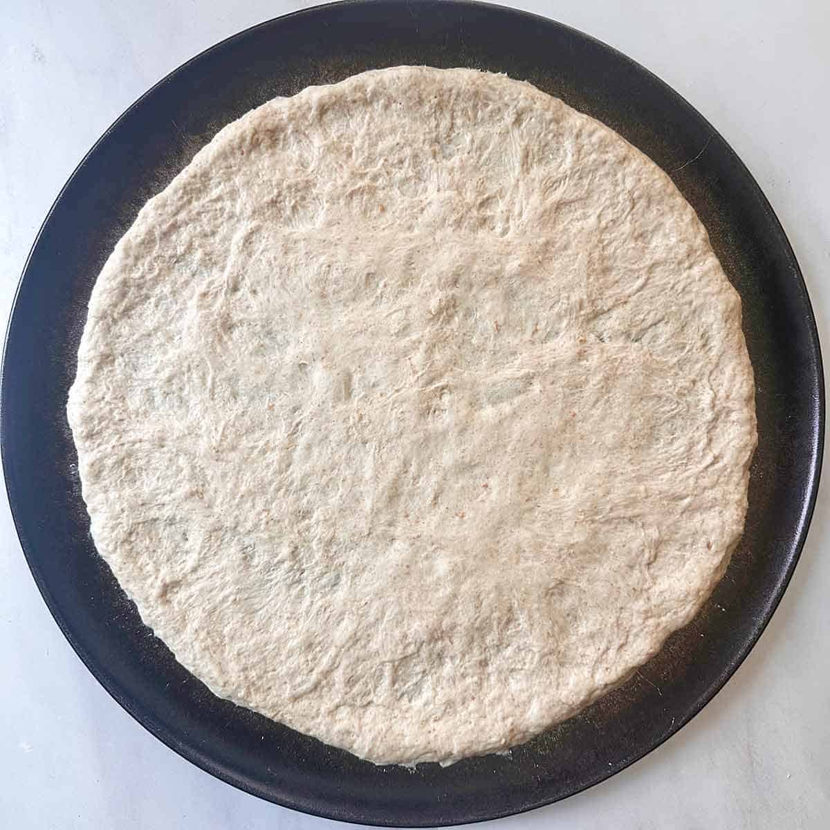 A round pizza pan with uncooked pizza dough.
