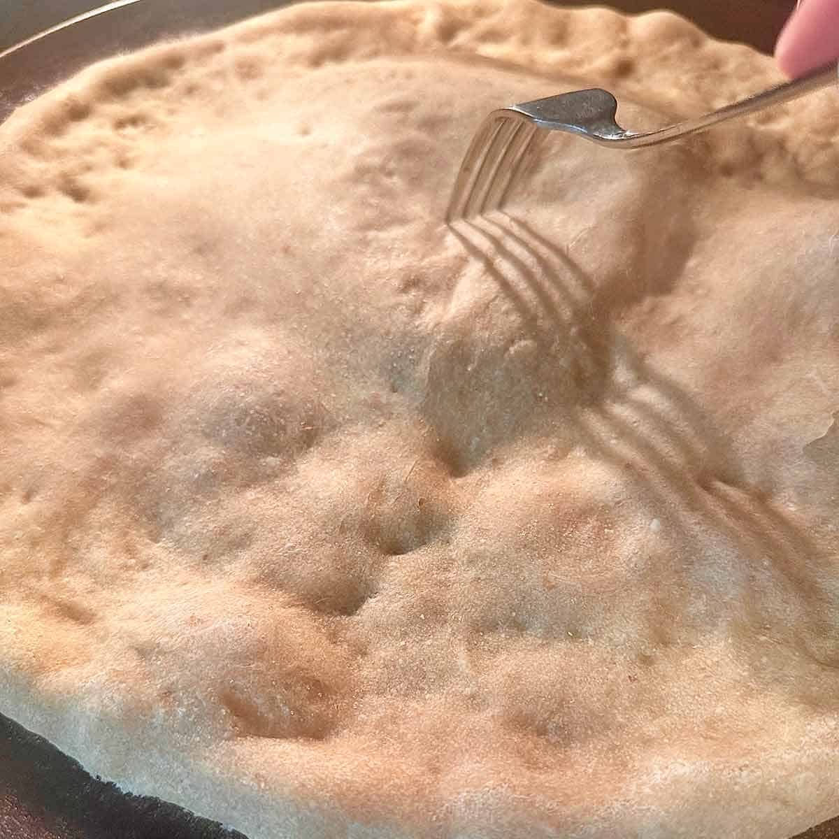 Poking an air bubble in a prebaked pizza crust with a fork.