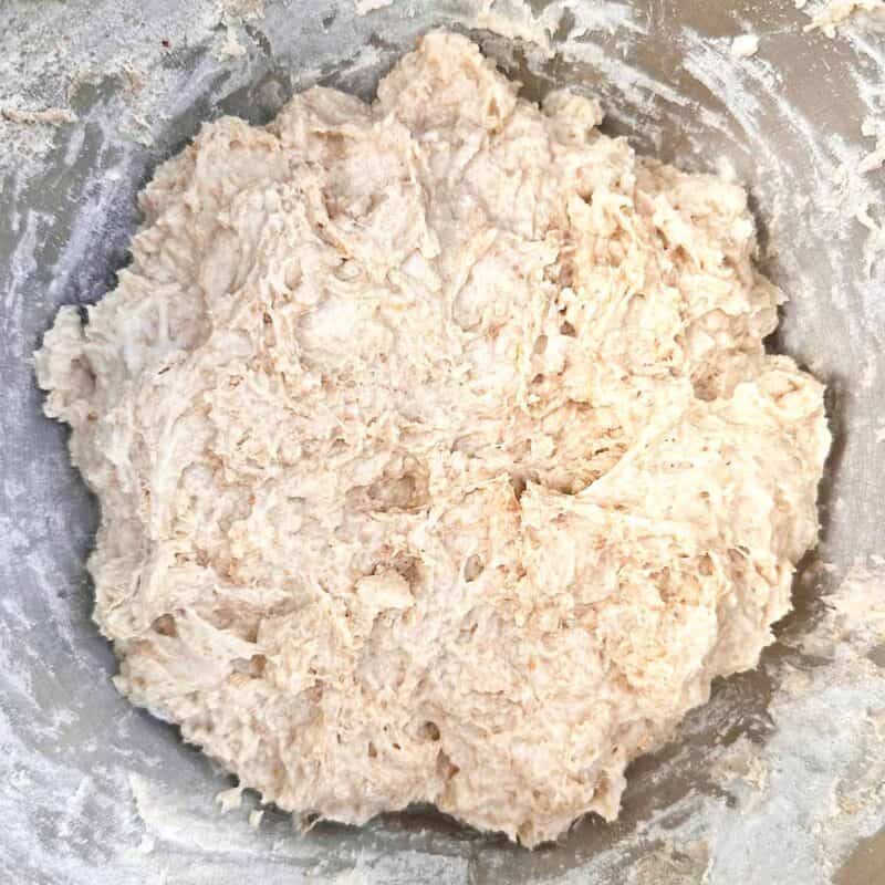 A mixing bowl with the ingredients for spelt flour pizza dough roughly mixed together.
