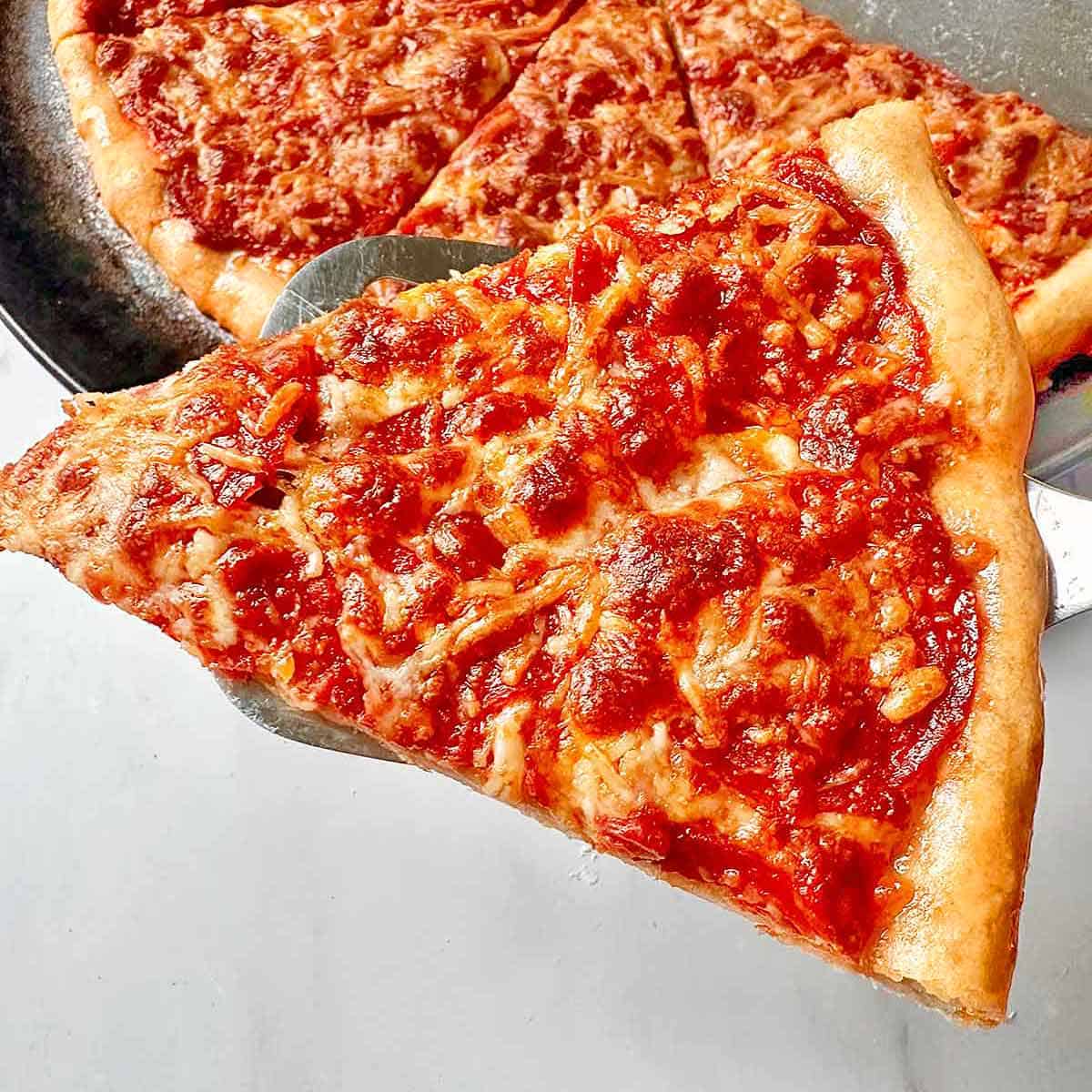 Serving a slice of hot homemade pepperoni pizza with a metal spatula.