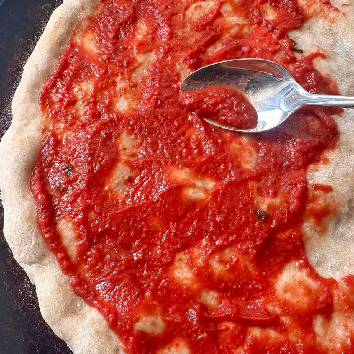 Spreading pizza sauce on the dough with a spoon.