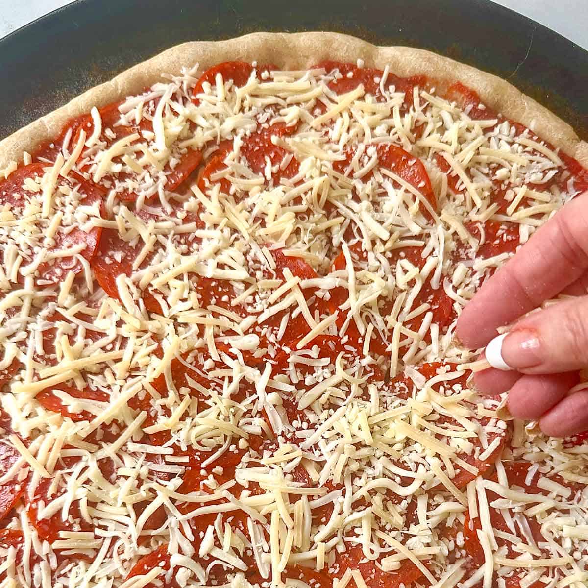 Adding a second layer of shredded cheese to the pepperoni pizza.