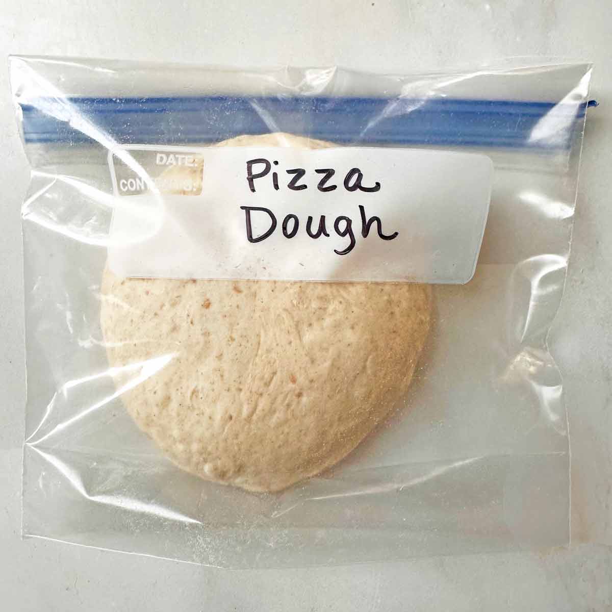 A ball of homemade spelt pizza dough in a zip top freezer bag.