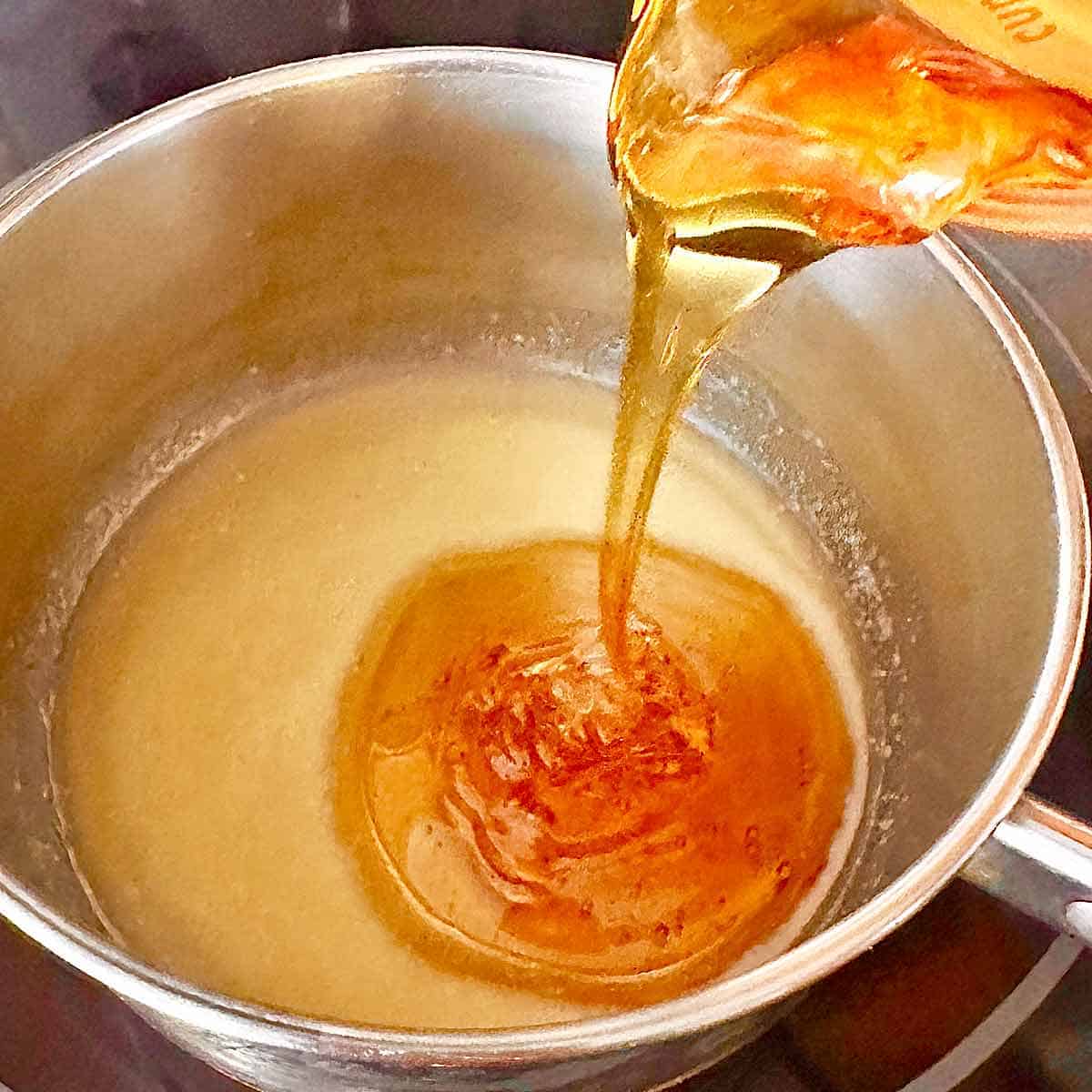 Adding honey to the melted butter and mustard in the saucepan.
