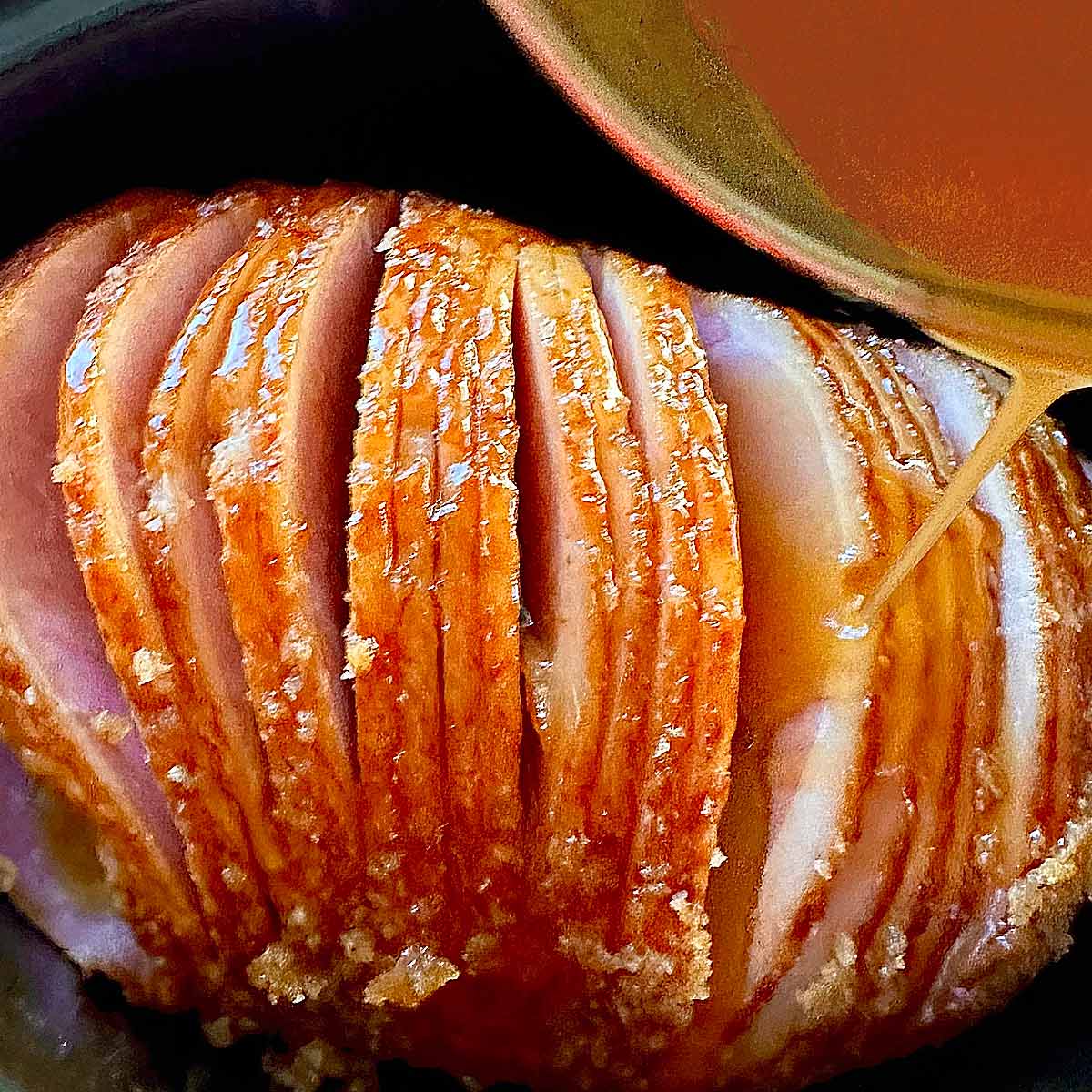 Drizzling the honey sauce glaze over the spiral ham slices of a Honey Baked Ham.
