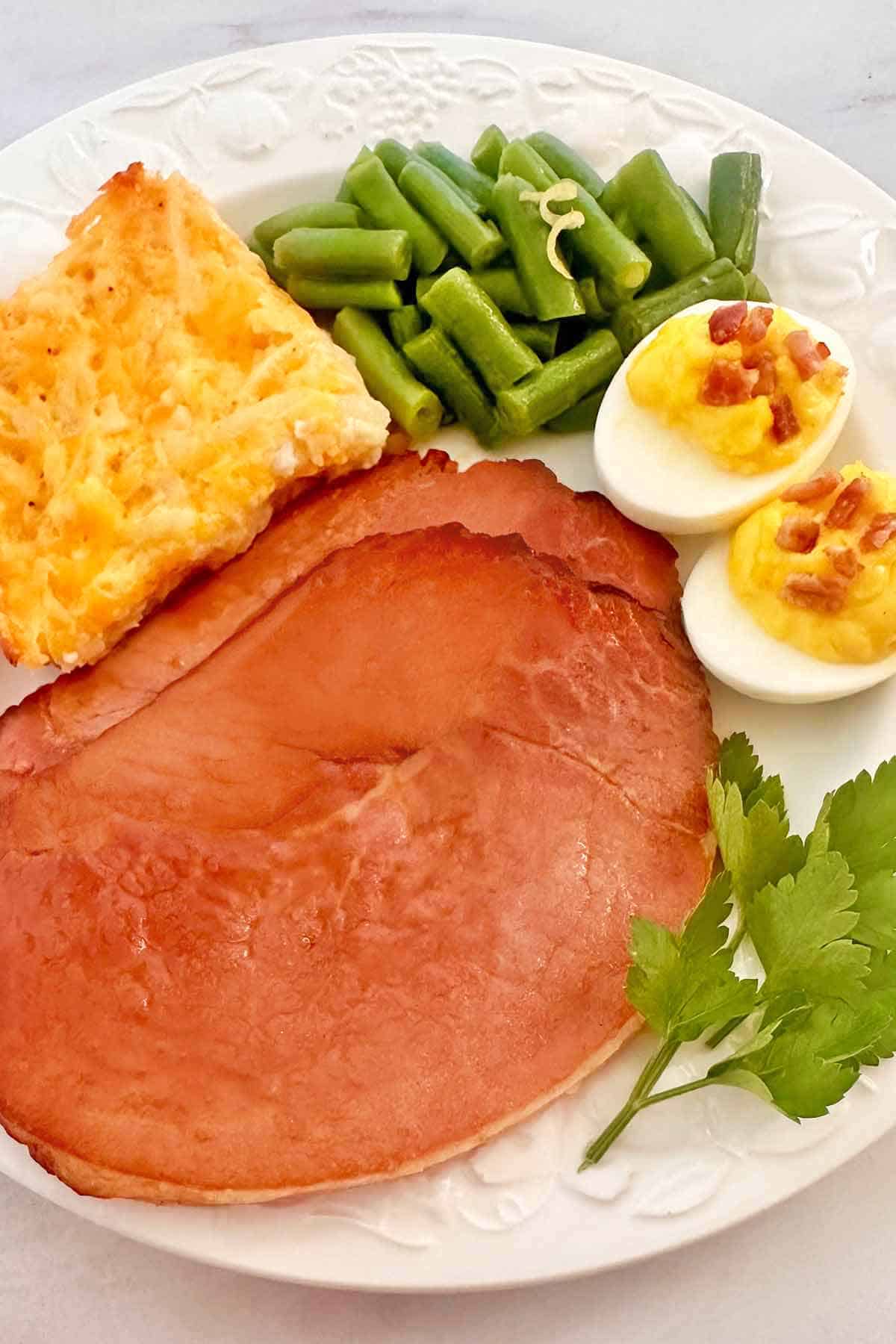 Two honey ham slices with deviled eggs, green beans, and potato casserole.