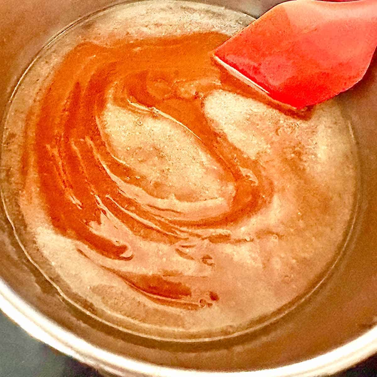 Combining the ingredients for honey ham glaze with a red spatula.